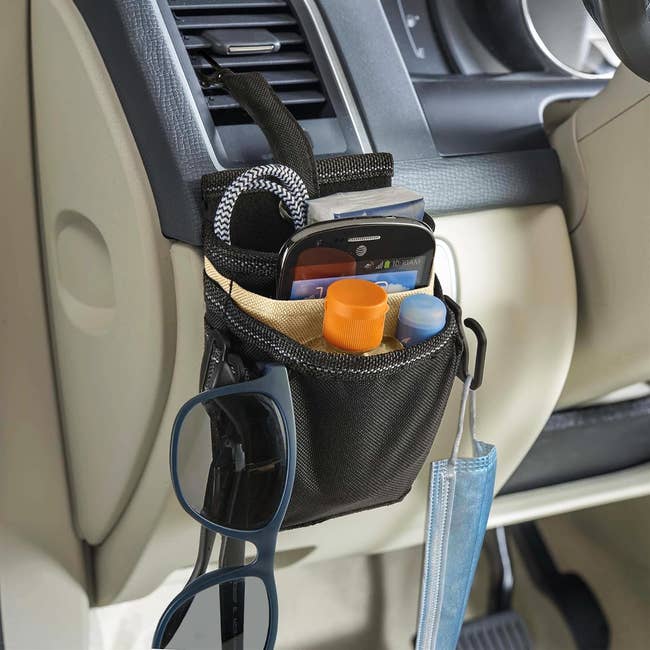 A small storage pouch holding items attached to a car via a clip on the air vent 