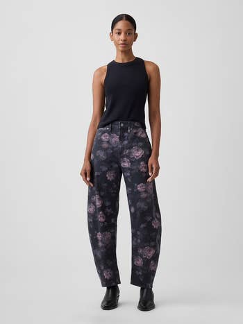 Person wearing a sleeveless apical and floral-patterned wide-leg pants with boots, lasting against a plain background