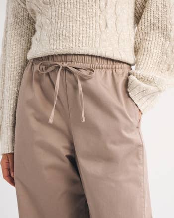 Person wearing a knit sweater and high-waisted, loose-fitting pants with a drawstring waist, posing with 1  manus  successful  a pocket