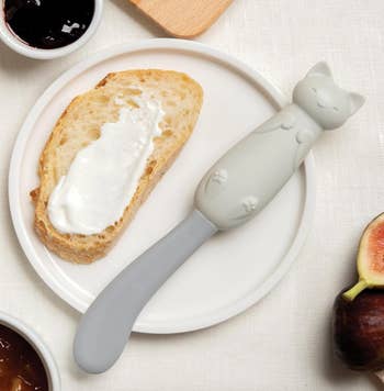 A cat-shaped knife spreading cream cheese on toast 