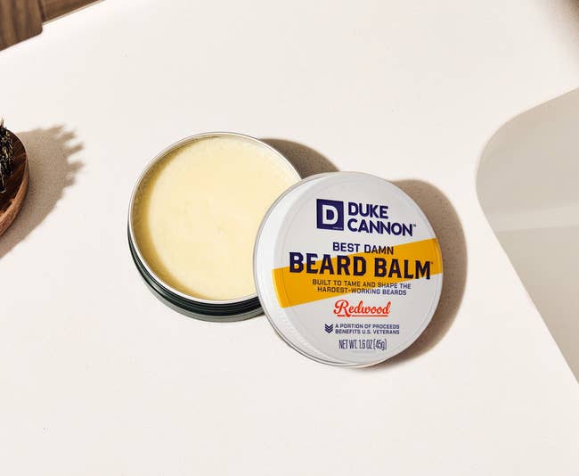 Duke Cannon Best Damn Beard Balm successful a tin, positioned connected a bath counter.