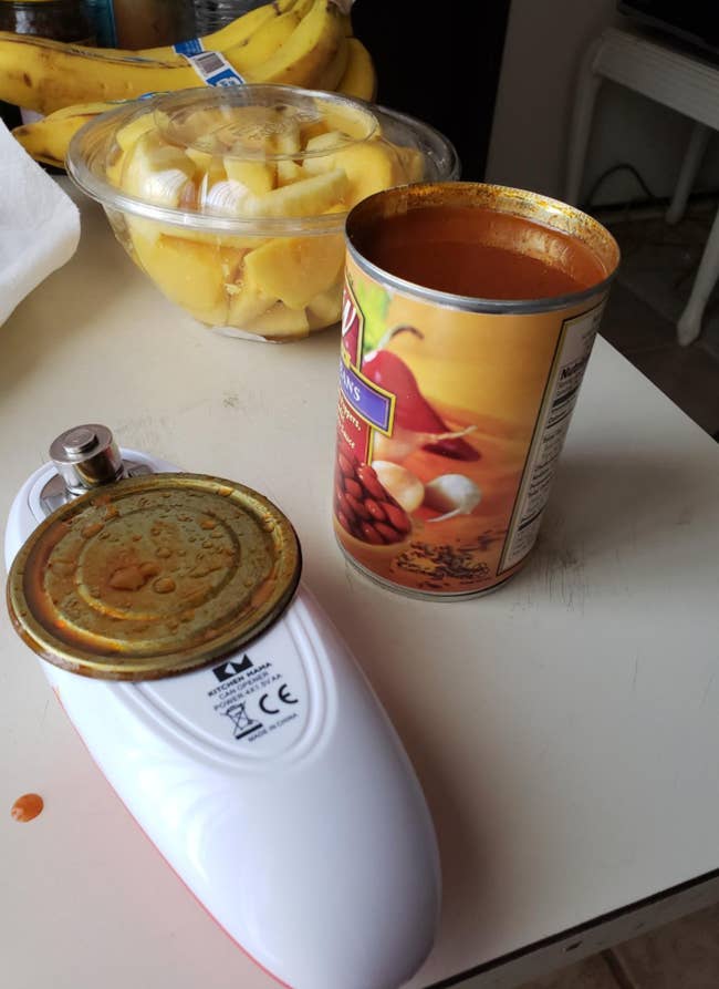 An open can next to the oval shaped can opening device with the lid stuck to it 