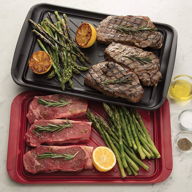 overhead shot of the red tray holding raw meats and vegetables and the black tray holding cooked ones next to some small seasoning bowls