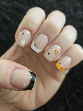 Close-up of a manus with Halloween-themed nail art, featuring ghosts, stars, and pumpkins connected short, quadrate nails against a acheronian background