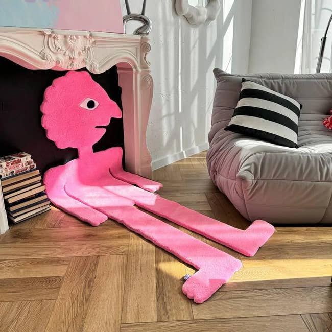 Quirky pinkish  level  mat shaped similar  a person, placed adjacent   a modern   sofa and books, adding an creator  interaction   to a stylish surviving  country   setting
