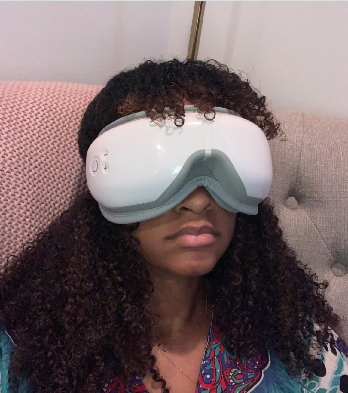 Reviewer wearing white eye massager with gray cushioning at the nose strapped around their head 