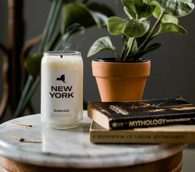 new york homesick candle on a table next to a plant and books