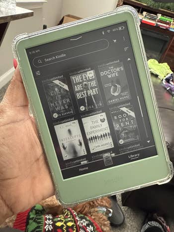 Person holding a Kindle displaying assorted  publication  titles, including 