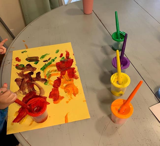 Child painting on paper with four cups of paint
