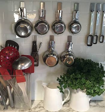 reviewer photo of the hooks holding measuring cups and spoons on a tiled wall