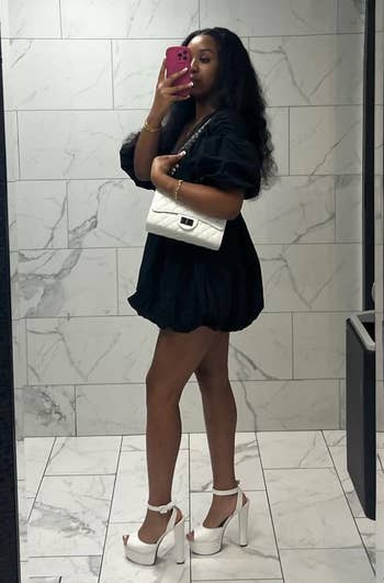 Person wearing a stylish abbreviated formal and precocious heels, holding a achromatic purse, takes a reflector selfie. Suitable for a buying article