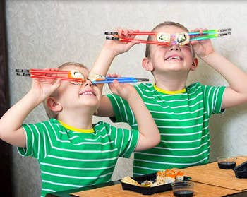 Two children holding sushi up to their eyes using the lightsaber chopsticks