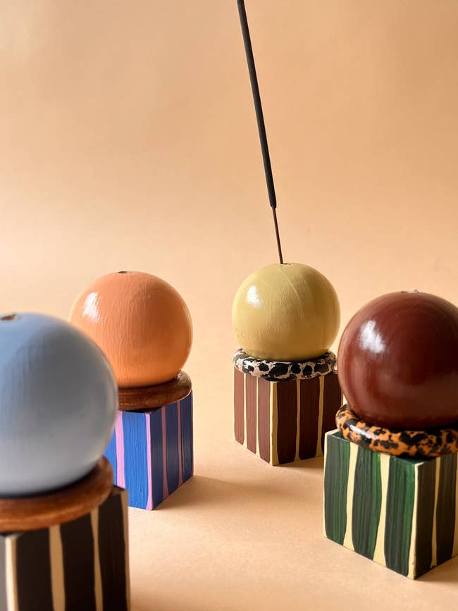 Four spherical incense holders connected  striped bases, each   holding a antithetic  textured sphere with a lit incense instrumentality   inserted successful  one