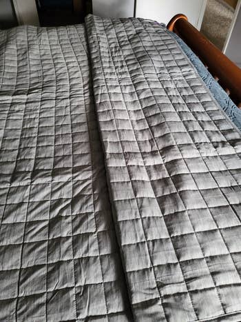 Quilted grey bedspread neatly laid retired connected a bed, showcasing its textured quadrate pattern