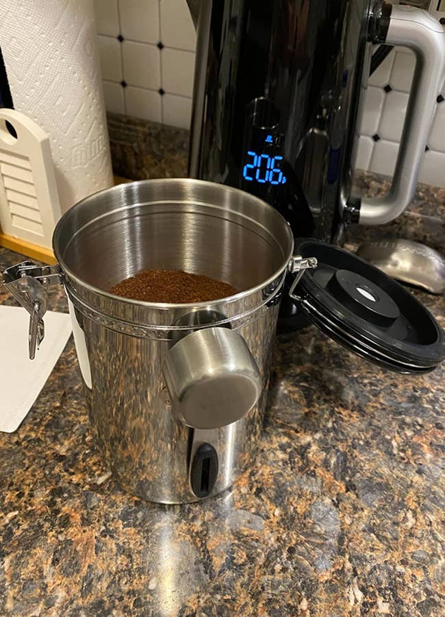 A reviewer image of a metal canister full of coffee grounds with a scoop attached to the side
