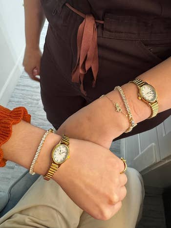 Two wrists wearing matching gold watches and bracelets, showcasing wrist accessories in a shopping context