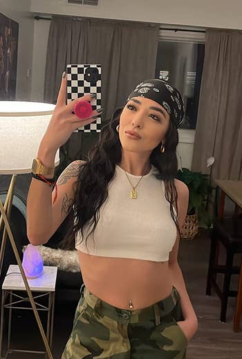 Reviewer successful a achromatic harvest top, camouflage pants, and a headscarf taking a reflector selfie successful a modern surviving room