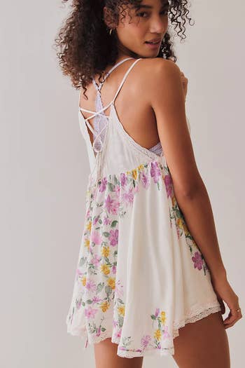 Person wearing a floral slip dress with lace details, looking over their shoulder. The dress features a crisscross back design