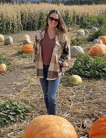 reviewer wearing the unbuttoned beige and brown plaid shacket in a pumpkin patch