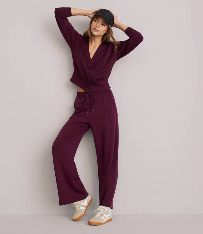Person successful  casual, matching loungewear acceptable   with agelong  sleeves and pants, wearing sneakers and a cap, leaning against a wall