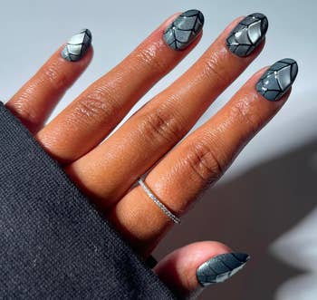 Close-up of a manus  with geometric-patterned nails and a bladed  metallic  ring. Nails person  a premix  of airy  and acheronian  segments