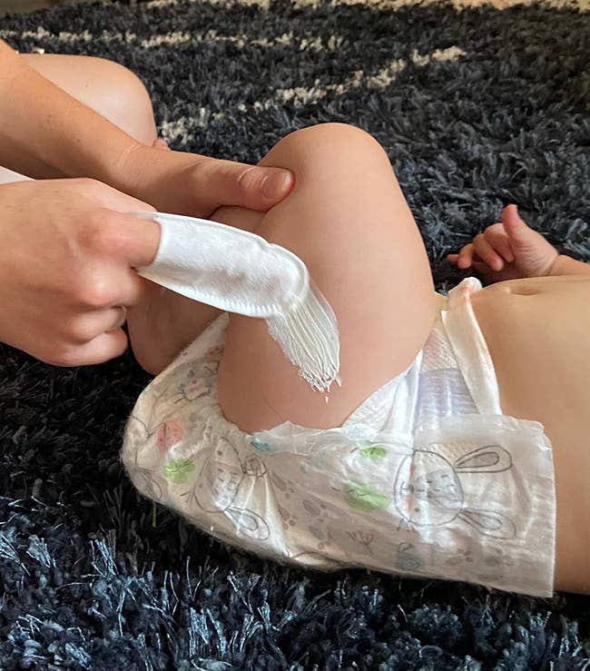 a reviewer using a finger shield wipe to apply lotion to their baby