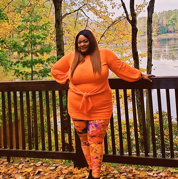 reviewer wearing the dress in orange, posing among fall foliage