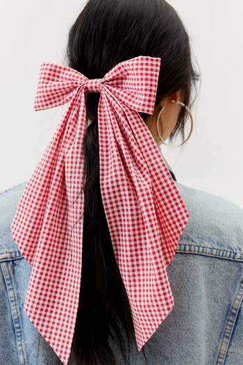 Person with a gingham bow in hair, seen from behind, on denim fabric background