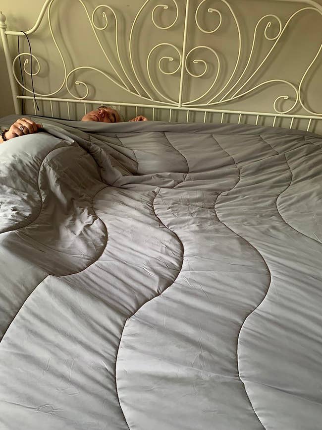 Person tucked in under a large comforter on an ornate metal bed, showcasing bedding style for a shopping feature