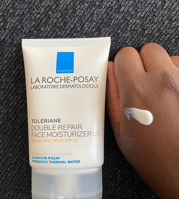 a tube of the moisturizing sunscreen next to a reviewer's hand, which has a dab of the product on it