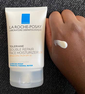 a tube of the moisturizing sunscreen next to a reviewer's hand, which has a dab of the product on it