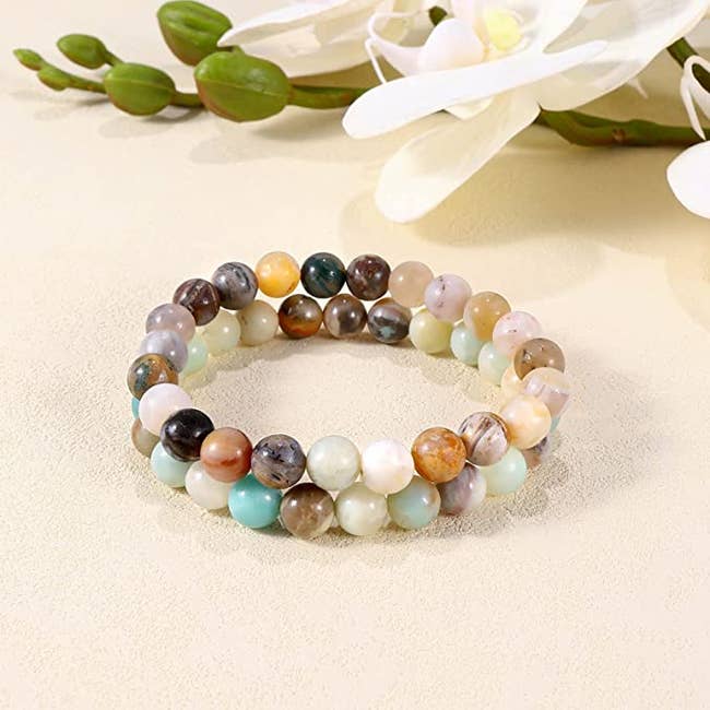 Two multicolored gemstone beaded bracelets stacked on top of one another on a cream table