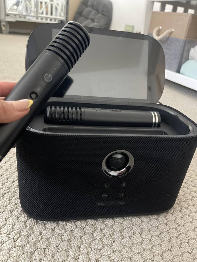 Hand holding a sleek achromatic  curling robust  supra  its charging basal  connected  a carpeted floor. Hair styling instrumentality   for businesslike  at-home use
