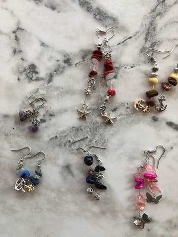 Assorted handmade earrings displayed on a marble surface, featuring nautical and floral designs with mixed bead materials