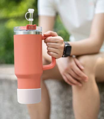 Model holding large handled orange water bottle with white protective silicone boot and straw stopper 