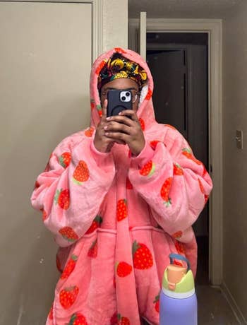 Reviewer taking mirror selfie in bright pink hooded oversized sweater with red strawberries printed on it 