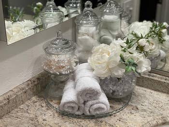 Bathroom vanity with jars of cotton products, rolled towels, and decorative flowers