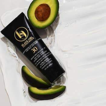 Skincare merchandise  conduit  with SPF 30 by Black Girl Sunscreen, surrounded by avocado slices connected  a textured surface