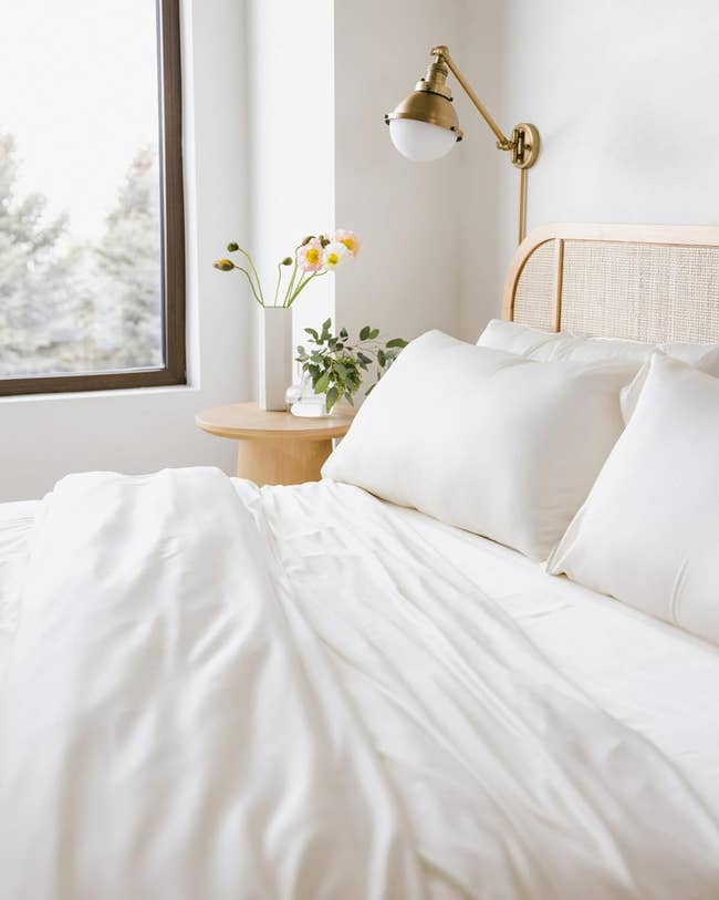 Cozy bedroom setup with a neatly made bed featuring white sheets, fluffy pillows, a round wooden nightstand, and a gold wall lamp