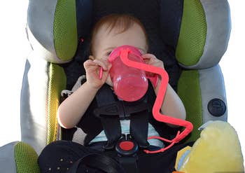 A baby drinking from a cup attached to a neon orange holder 