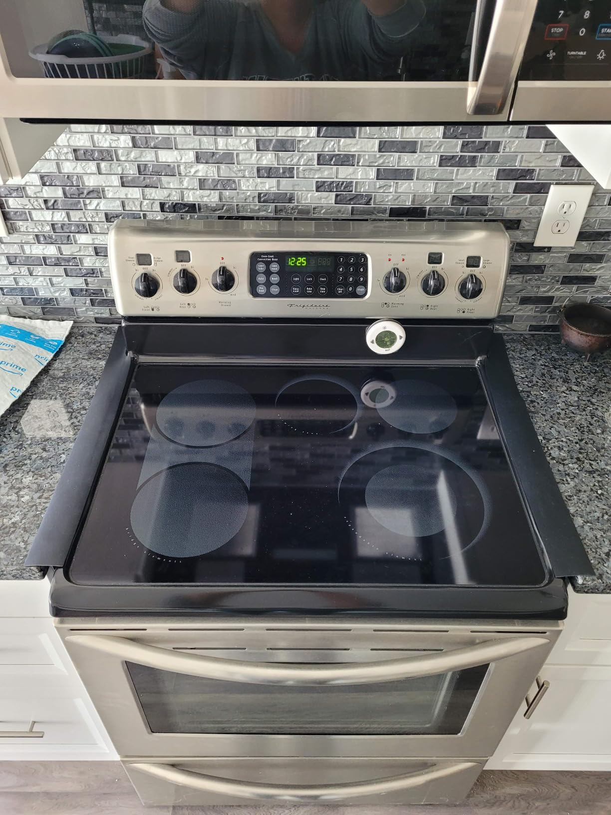 Dapur modern dengan kompor listrik stainless steel, menampilkan jam digital, kenop kontrol, dan kompor kaca halus