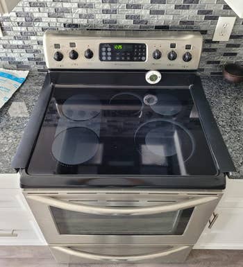 Dapur modern dengan kompor listrik stainless steel, menampilkan jam digital, kenop kontrol, dan kompor kaca halus
