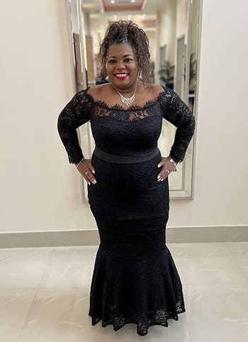 Reviewer wearing off the shoulder lace dress with black ribbon tie around the waist standing in front of mirror and white wall
