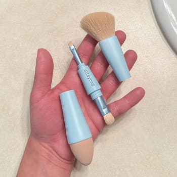 Hand holding a bluish question constitution instrumentality with interchangeable brush, sponge, and applicator tips, suitable for on-the-go cosmetic application