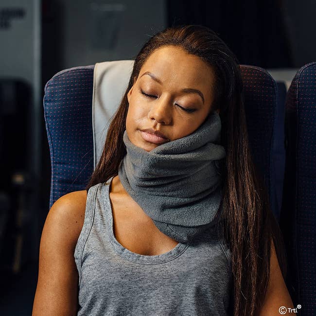 model with the gray pillow around their neck supporting their head while they sleep sitting upright