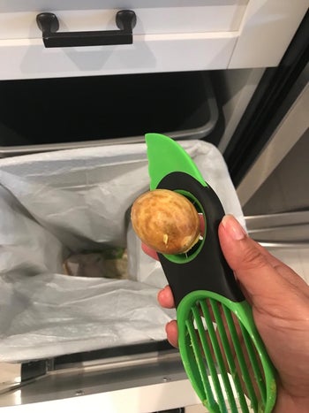 A reviewer with the pitting part of the tool holding an avocado pit