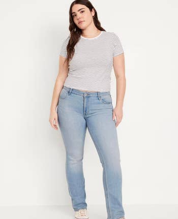 A model stands facing forward wearing a white striped t-shirt, light blue jeans, and beige sneakers