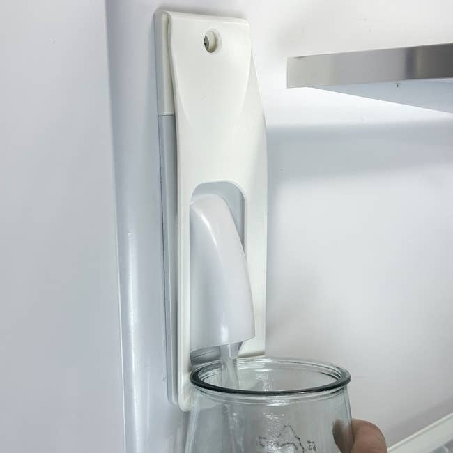 A person filling a glass with water from a refrigerator's dispenser