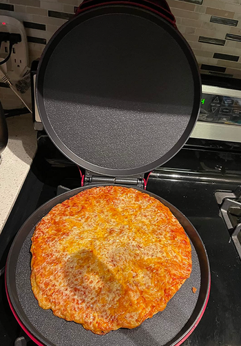 A small round grilling surface with an open lid cooking a cheese pizza 