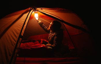 camper hanging lantern onto top of dark tent